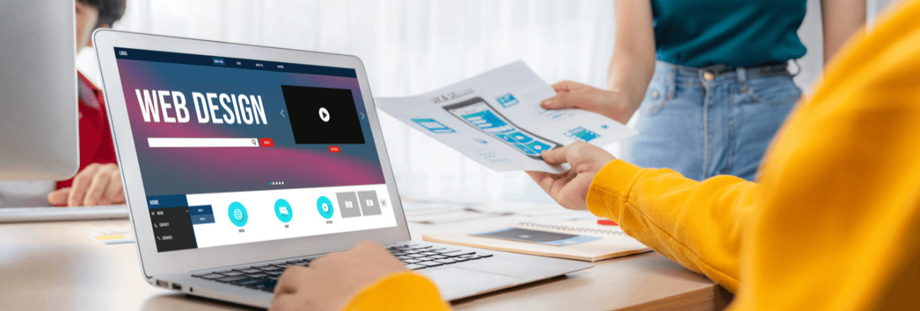 Designer reviews UI wireframes beside a laptop showing “Web Design"