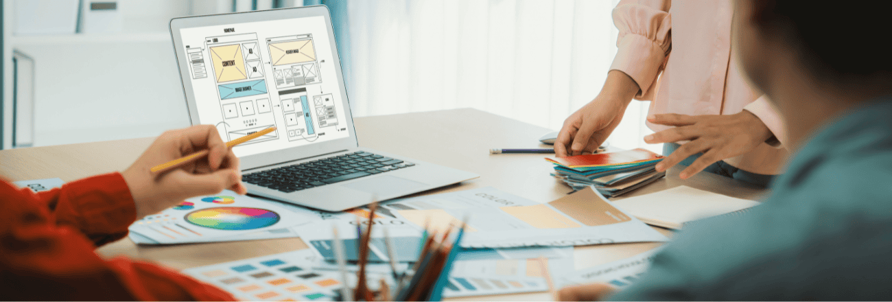 Team reviewing UX wireframes on a laptop with color swatches on the table.